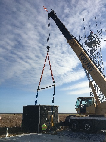 Crane setting an equipment shelter at a job site